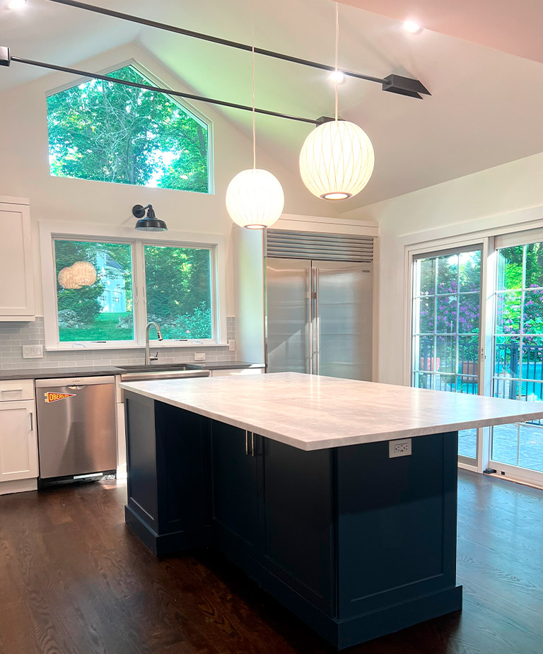 A detailed shot of a kitchen remodeling project featuring white shaker cabinets, gold hardware, a custom wood-trim range hood, and a decorative tile backsplash.