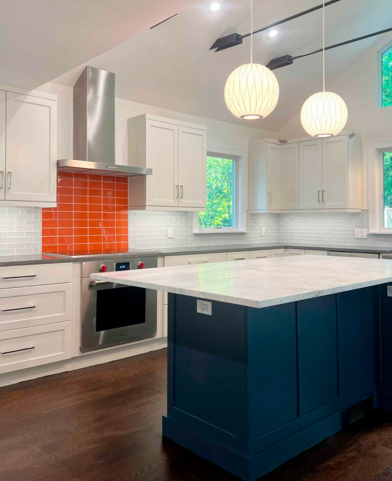 A stunning kitchen remodeling project featuring a deep navy blue central island, white shaker cabinets, and a vibrant orange tile backsplash for a modern pop of color.