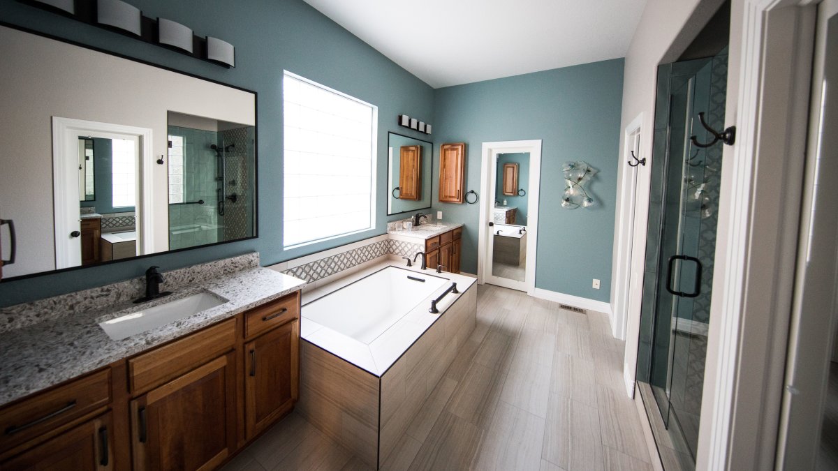 Spacious modern master bathroom with freestanding bathtub, wooden cabinets, and granite countertops.