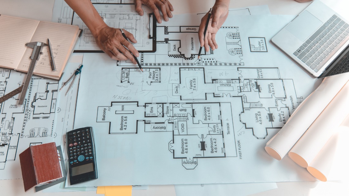 working on blueprints with a laptop, calculator, and drawing tools