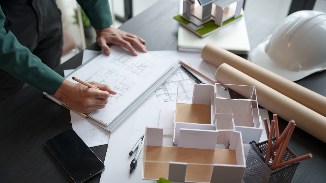 sketching on blueprints at a desk with architectural models