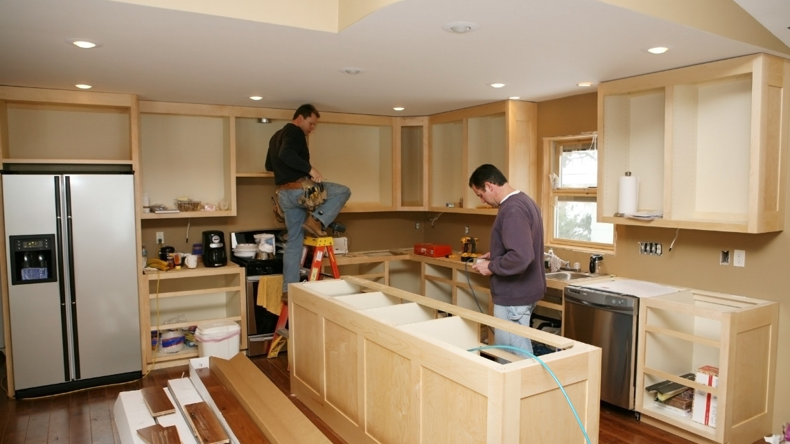 two contractors installing light wood kitchen cabinets