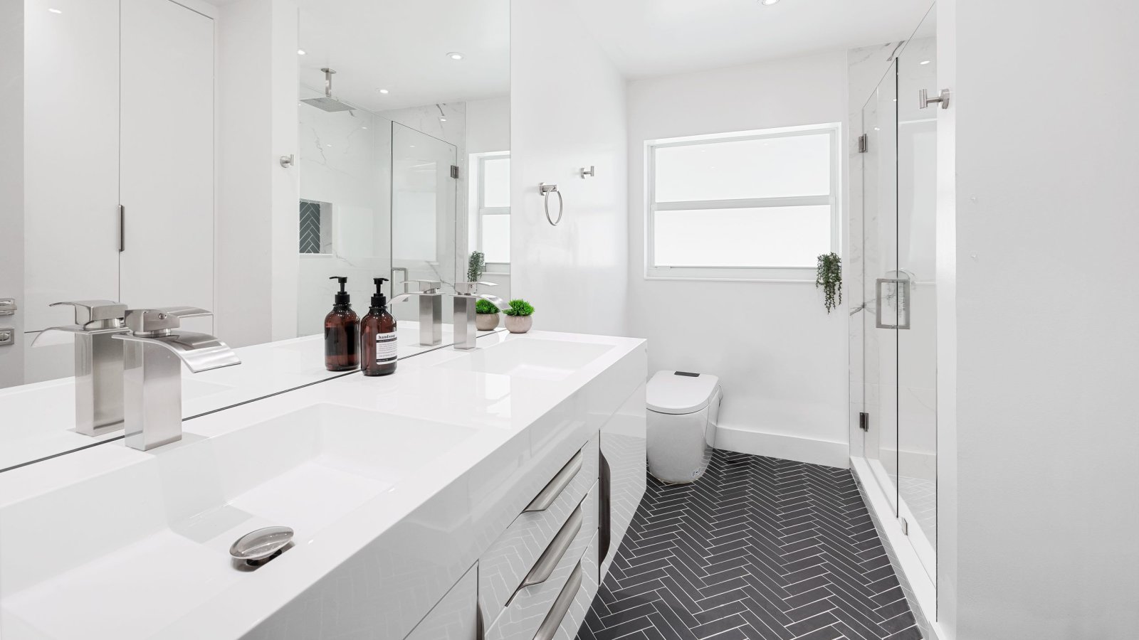 Modern white bathroom featuring sleek fixtures and elegant herringbone flooring design.